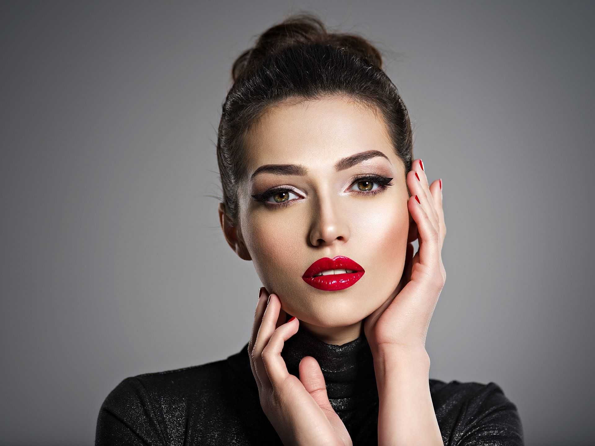 Woman with bold makeup posing with hands on face.